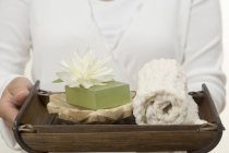 Closeup view of woman holding soap, water lily and towel on tray — Stock Photo