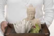 Woman holding statue of Buddha, candle and orchid on tray — Stock Photo