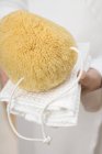 Mani che tengono spugna da bagno su asciugamano bianco — Foto stock