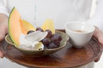 Primo piano vista ritagliata di persona che tiene piatto di frutta e tè ciotola sul vassoio — Foto stock