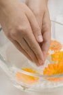 Closeup view of woman dipping hands in soapy water with marigolds — Stock Photo