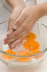 Donna che si lava le mani in acqua saponata con calendule — Foto stock
