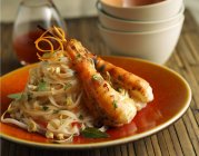Vue rapprochée des crevettes thaïlandaises avec des nouilles sur plaque orange — Photo de stock