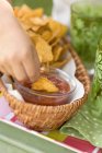 Nahaufnahme der Hand, die Tortilla-Chips in Salsa taucht — Stockfoto