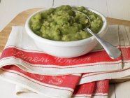 A dish of mushy peas on a tea towel in white dish with spoon over towel — Stock Photo