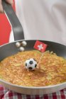 Poêle à frire main avec rsti, football jouet & drapeau suisse — Photo de stock