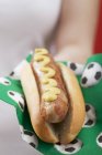 Hand holding hot dog with mustard — Stock Photo