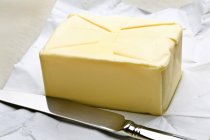 Vista close-up de bloco de manteiga com faca no papel — Fotografia de Stock
