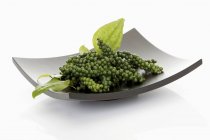 Clusters of green peppercorns with leaves in dish — Stock Photo
