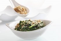 Spinaci con semi di sesamo tostati su piatto bianco con cucchiaio — Foto stock