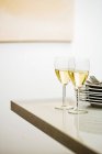 Glasses of white wine beside pile of plates — Stock Photo