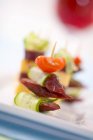Fette di salsiccia, cetriolo e pomodoro su bastoncino da cocktail su piatto bianco — Foto stock