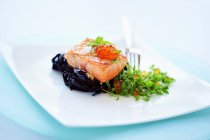 Fried salmon on black tagliatelle — Stock Photo