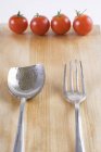 Old cutlery and four cherry tomatoes on wooden surface — Stock Photo