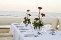 Vue de jour de la table dressée avec oeillets rouges sur la plage — Photo de stock