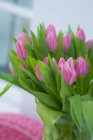 Вид на стеклянную вазу из розовых тюльпанов и зеленых листьев — стоковое фото