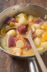 Картофельное и овощное рагу с тунцом в металлической сковороде с деревянной ложкой — стоковое фото