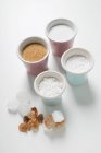 Vários tipos de açúcar em gorros e na superfície branca — Fotografia de Stock