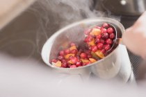 Closeup view of boiling cranberries and oranges in pot with spoon — Stock Photo