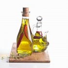 Olio di peperoncino e con erbe aromatiche in due caraffe di vetro su tavola di legno — Foto stock