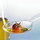 Cocktail tomato with oil on spoon on blue background — Stock Photo