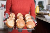 Cropped view of woman holding freshly baked popovers on a rack — Stock Photo