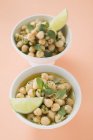 Chick-peas with lime wedges and herbs in bowls over pink surface — Stock Photo