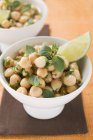 Chick-peas with lime wedges and herbs in white bowl — Stock Photo