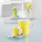 Nahaufnahme von gelben Tassen mit Keksen auf weißer reflektierender Oberfläche — Stockfoto