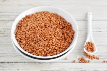 Closeup view of red lentils in bowls, on spoon and wooden surface — Stock Photo