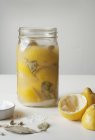 Vista de cerca de limones conservados en un frasco de vidrio con sal, vainas de cardomomo y hojas de laurel - foto de stock