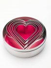 Closeup view of heart-shaped cookie cutters in round metal tin on white surface — Stock Photo