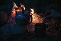 Рука перемішуючи чай в чашці чайника біля багаття табору — стокове фото