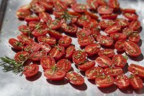 Tomates fraîches coupées en deux avec romarin — Photo de stock