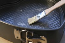 Closeup view of greasing a baking tin with a brush — Stock Photo