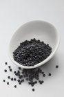 Closeup view of beluga lentils in bowl and on white surface — Stock Photo