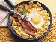 Fried egg and bacon on chick-peas in pan with fork — Stock Photo