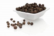 Closeup view of allspice berries in a bowl and on white surface — Stock Photo