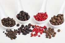 Vue rapprochée des baies de piment avec poivre rose, baies de genièvre et grains de poivre noir sur cuillères — Photo de stock