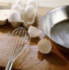 Eggshells and whisk on table — Stock Photo