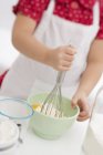 Tilted view of girl mixing egg, flour and butter with whisk — Stock Photo