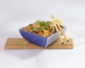 Pollo con limón, cebolla y cilantro en tazón azul sobre estera de paja - foto de stock