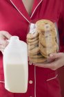 Primer plano vista recortada de la mujer sosteniendo vaso de galletas de arándano y botella de leche - foto de stock