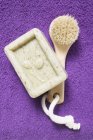 Vista dall'alto del sapone d'oliva e spazzola su asciugamano di spugna viola — Foto stock