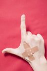 Hand with crossed sticking plasters on red surface showing thumb and pointing fingers — Stock Photo