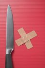 Knife and crossed sticking plasters on red striped surface — Stock Photo