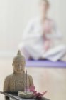 Estátua de Buda e fumar incenso vara com mulher sentada de pernas cruzadas no fundo — Fotografia de Stock