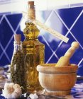 Vista ravvicinata dell'aglio con bottiglia di capperi, bottiglia di olio di mandorle, malta di legno e pestello — Foto stock