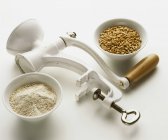 Closeup view of manually-operated cereal mill with grains on white background — Stock Photo