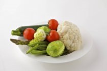 Асорті овочі на тарілці на білому тлі — стокове фото
